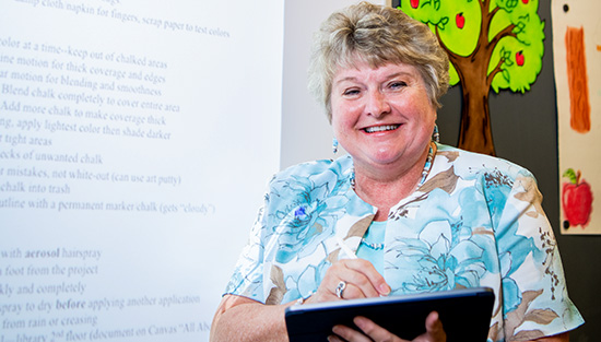 Teacher standing by a projector screen holding a tablet