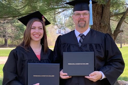 Alumni Scot Bryan and his daughter showing their diplomas at graduation